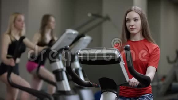 穿红色衬衫的可爱女孩在运动自行车上大力工作只是在新的健身房里工作视频的预览图