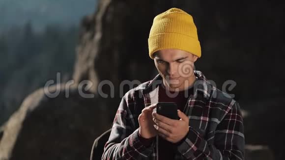 年轻的快乐男人和一个人在美丽的山前站在岩石的顶端的电话聊天通信视频的预览图