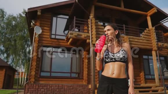 运动的女人在一个木制豪宅的背景下一个漂亮的压在黑色顶部的美女锻炼了饮用水视频的预览图