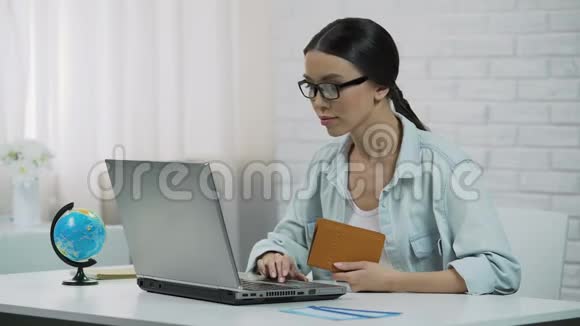 亚洲女孩在笔记本电脑上输入护照数据在旅行社预订旅游视频的预览图