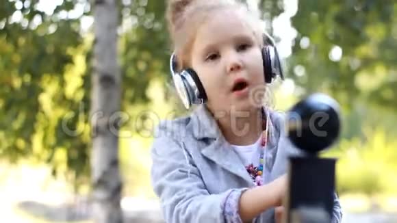 可爱的女孩戴着耳机听音乐在公园里用桦树唱歌视频的预览图