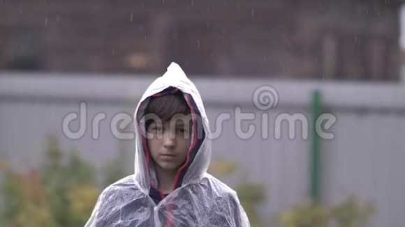 悲伤沮丧的男孩站在雨中的雨衣里慢动作视频的预览图