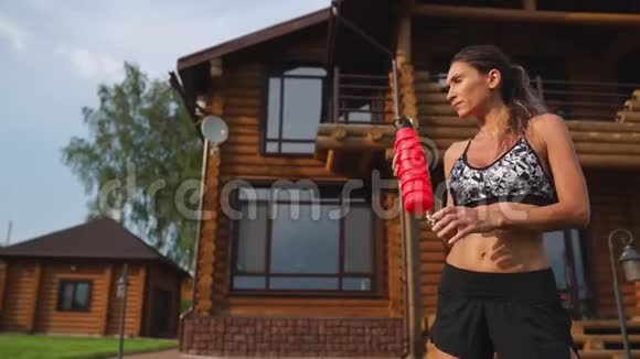 曲线深色皮肤腹部肌肉膨胀在大房子的背景下锻炼后饮用蛋白质视频的预览图