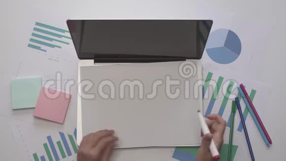 女人在笔记本电脑上的一张纸上写内容带有图表的办公桌面视频的预览图
