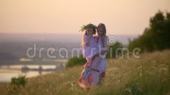 年轻的母亲抱着女儿在夏日的夕阳下走下山视频的预览图