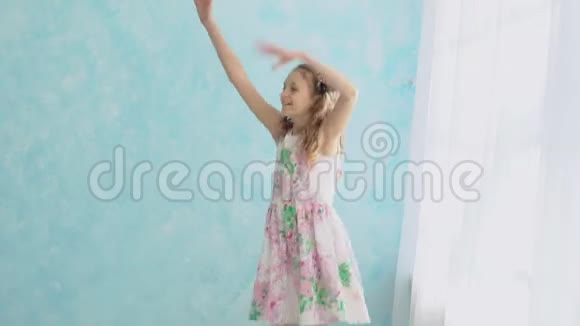 穿着一件漂亮花裙的女孩正在窗前一面蓝色墙的背景下跳舞视频的预览图