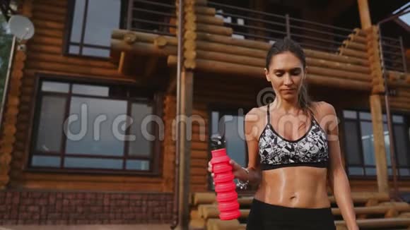 运动的女人在一个木制豪宅的背景下一个漂亮的压在黑色顶部的美女锻炼了饮用水视频的预览图