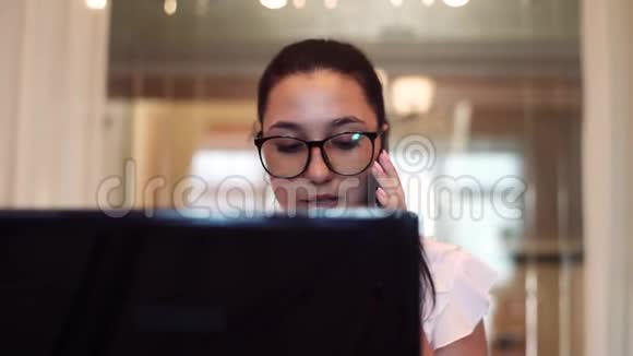 戴眼镜的女商人用电脑和手机工作坐在办公室的桌子上心情很好特写镜头视频的预览图