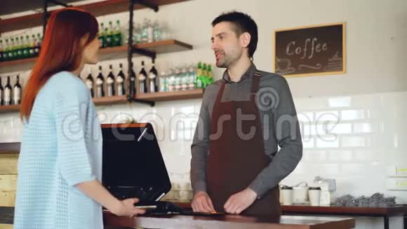 迷人的年轻女子正在和友好的男收银员交谈她们在咖啡店用手机支付外卖咖啡的费用视频的预览图
