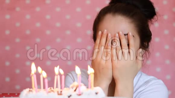 年轻女子许愿在聚会上吹灭生日蛋糕上的蜡烛粉色背景特写视频的预览图