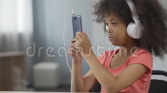 严肃的非裔美国人孩子戴着耳机用手机看视频视频的预览图