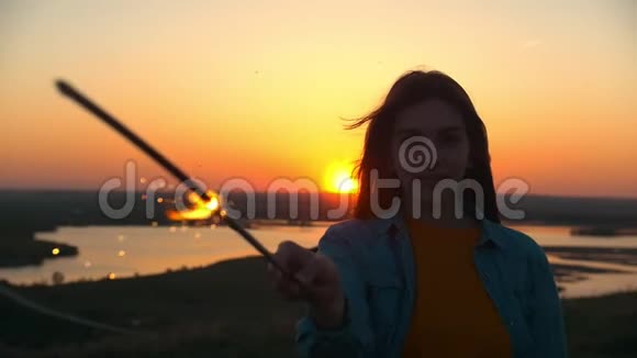 微笑的年轻女子举着星星之火站在夕阳的山上视频的预览图