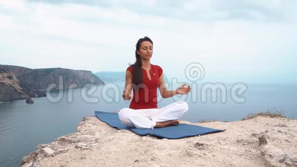 女孩坐在海边的岩石上冥想莲花瑜伽姿势集中注意力放松心灵灵魂和身体视频的预览图