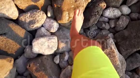 一个光着脚在岩石海滩上散步的人他的旅行和海上度假理念视频的预览图