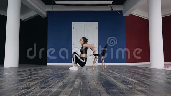 运动女孩用蹲着的双手绕在椅子上进行练习年轻的健身女子训练表演视频的预览图