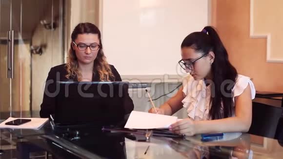 两个戴着眼镜的女商人穿着商务服装在办公室里的一个商务项目上工作坐在桌子旁视频的预览图