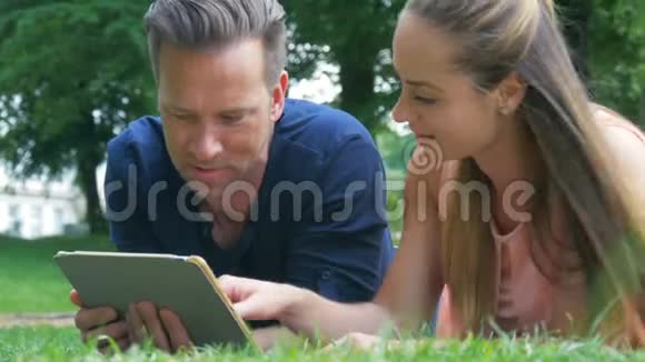 一对夫妇在公园里不寒而栗在他们的平板电脑上看照片并在社交网络上发布视频的预览图