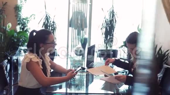 两个商务女性在一间漂亮的办公室里坐在桌子旁互相使用一个商务项目视频的预览图