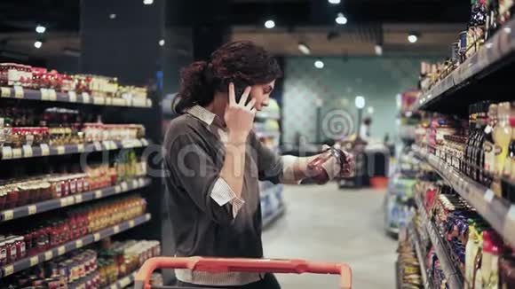 美丽的女性买家试图在杂货店选择产品同时与某人在电话中交谈视频的预览图