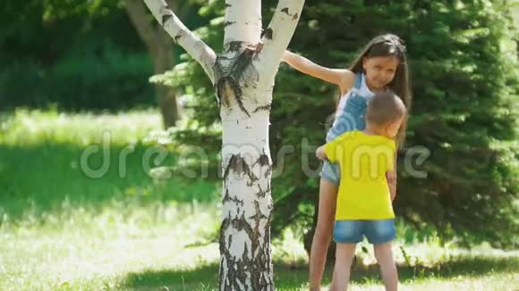 可爱的女孩和弟弟在阳光明媚的日子里在树上跑来跑去玩视频的预览图