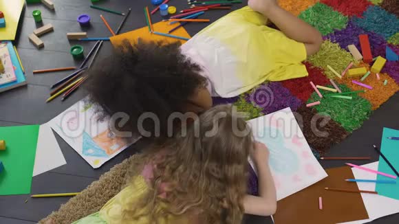 蜷缩的女孩子躺在地板上在幼儿园用彩色铅笔画画视频的预览图