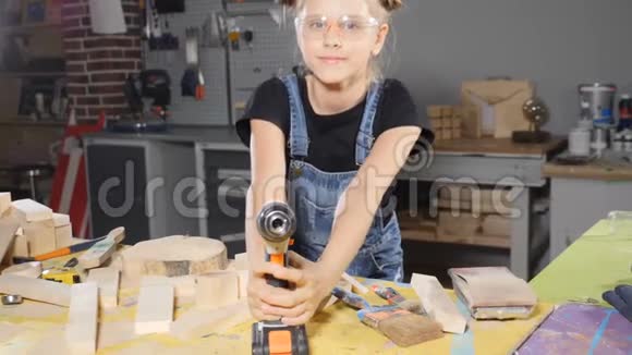 一幅有趣的10岁女孩的画像她穿着木工拿着一台电子钻对着镜头摆姿势小建筑视频的预览图