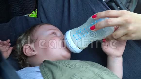 婴儿从奶瓶中吸奶母亲在公园里喂婴儿牛奶视频的预览图