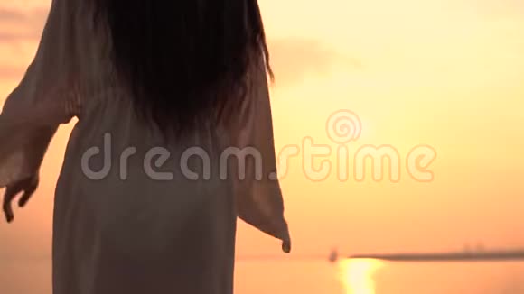 一个穿着沙滩裙的女孩站在夕阳的背景上双手朝不同的方向伸展视频的预览图