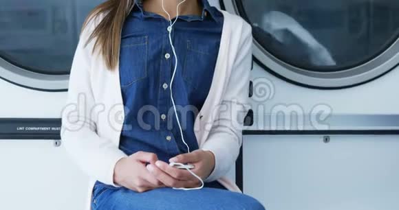 女子在自助洗衣店4k手机听音乐视频的预览图