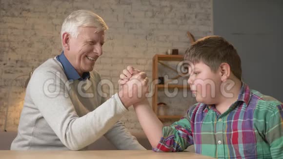 祖父和孙子在家里舒适的房间里摔跤在手臂摔跤中测量力量小胖孩子视频的预览图