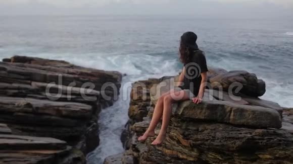 那个女孩坐在靠近海洋的岩石上视频的预览图