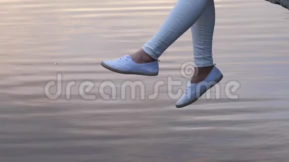日落时分女人在平静的水面上摆动双腿视频的预览图