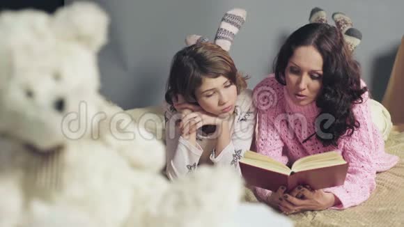 妈妈和女儿舒服地躺在床上读童话故事做梦视频的预览图
