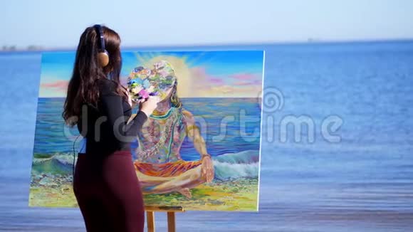 夏天河边沙滩上日出时一位美丽的女艺术家手里拿着画笔调色板画画视频的预览图