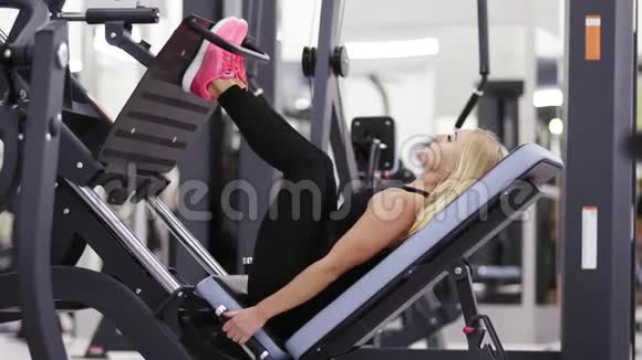 漂亮的女孩穿着黑色运动服在健身房的腿部按压马什尼上做运动保健和福利视频的预览图