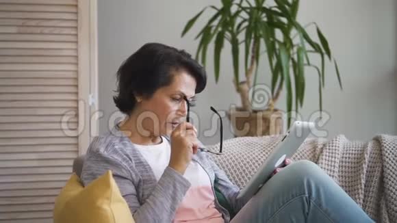 有魅力的老妇人在家里用平板电脑上网视频的预览图