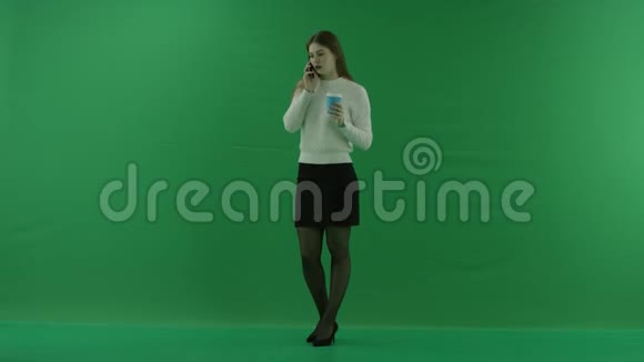 女孩站在半个转弯处看着左边打电话从绿色屏幕上的玻璃杯里喝东西视频的预览图