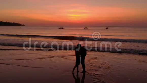一对年轻夫妇在日落时分与儿子在附近奔跑接吻的慢镜头视频的预览图