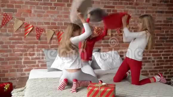 三胞姐妹穿着睡衣在家里的床上打枕头战卧室是圣诞节装饰的视频的预览图