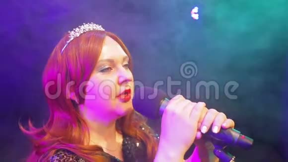 年轻的红发女歌手在台上的麦克风前冒着烟唱歌视频的预览图