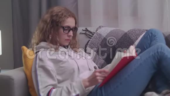 年轻的美女晚上在她舒适的客厅里读一本纸书视频的预览图