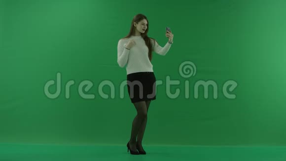 女孩站在一个半转弯看着右边在绿色屏幕上自拍视频的预览图
