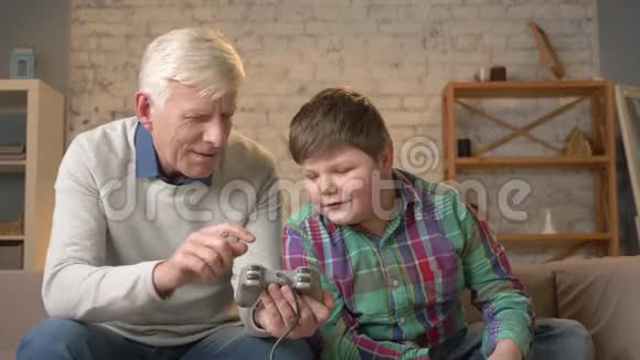 孙子教爷爷玩控制台游戏一位老人正在学习如何玩一个打斗的电子游戏视频的预览图