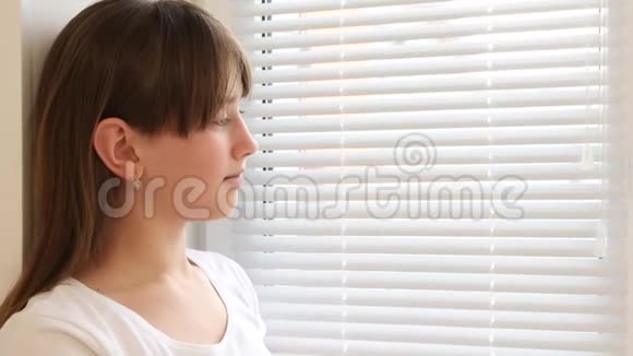 悲伤的女孩透过窗户透过百叶窗和微笑视频的预览图