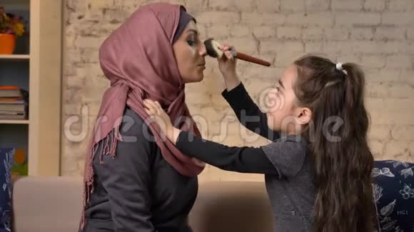 小女孩给她的穆斯林妈妈做了一个头巾的化妆化妆刷笑微笑的家庭懒散家庭舒适视频的预览图