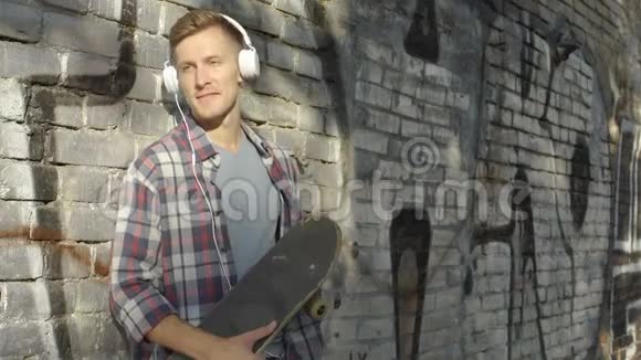 有滑板的帅哥在智能手机上听最喜欢的音乐视频的预览图