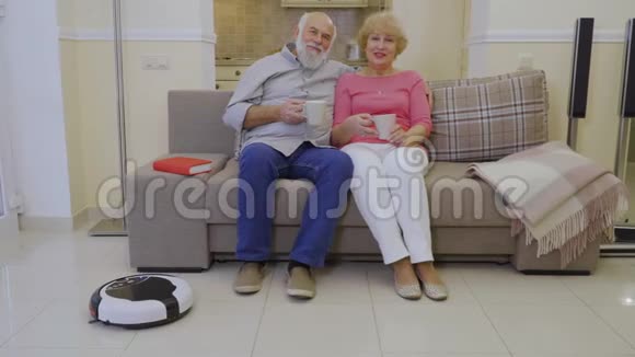 在自动机器人清洁客厅地板的过程中老夫妇在沙发上放松视频的预览图