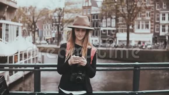 在桥上用智能手机的漂亮女人4K年轻的女士戴着时尚的帽子长发和相机类型的信息视频的预览图