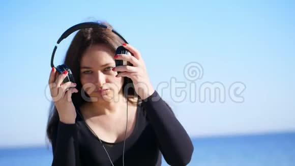 夏天在大海的背景下美丽的女人留着长长的黑发戴着大耳机听着视频的预览图