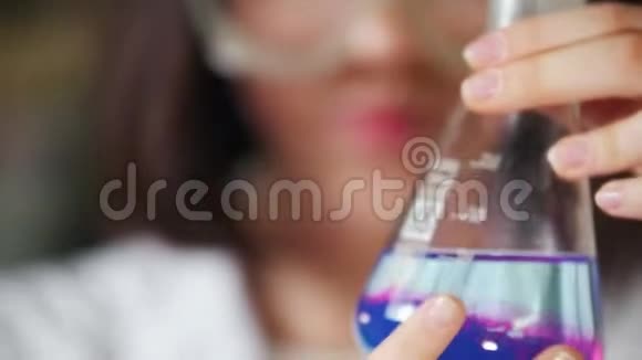 化学实验室里的年轻女子拿着一个蓝色和紫色的瓶子把注意力集中在烧瓶上视频的预览图